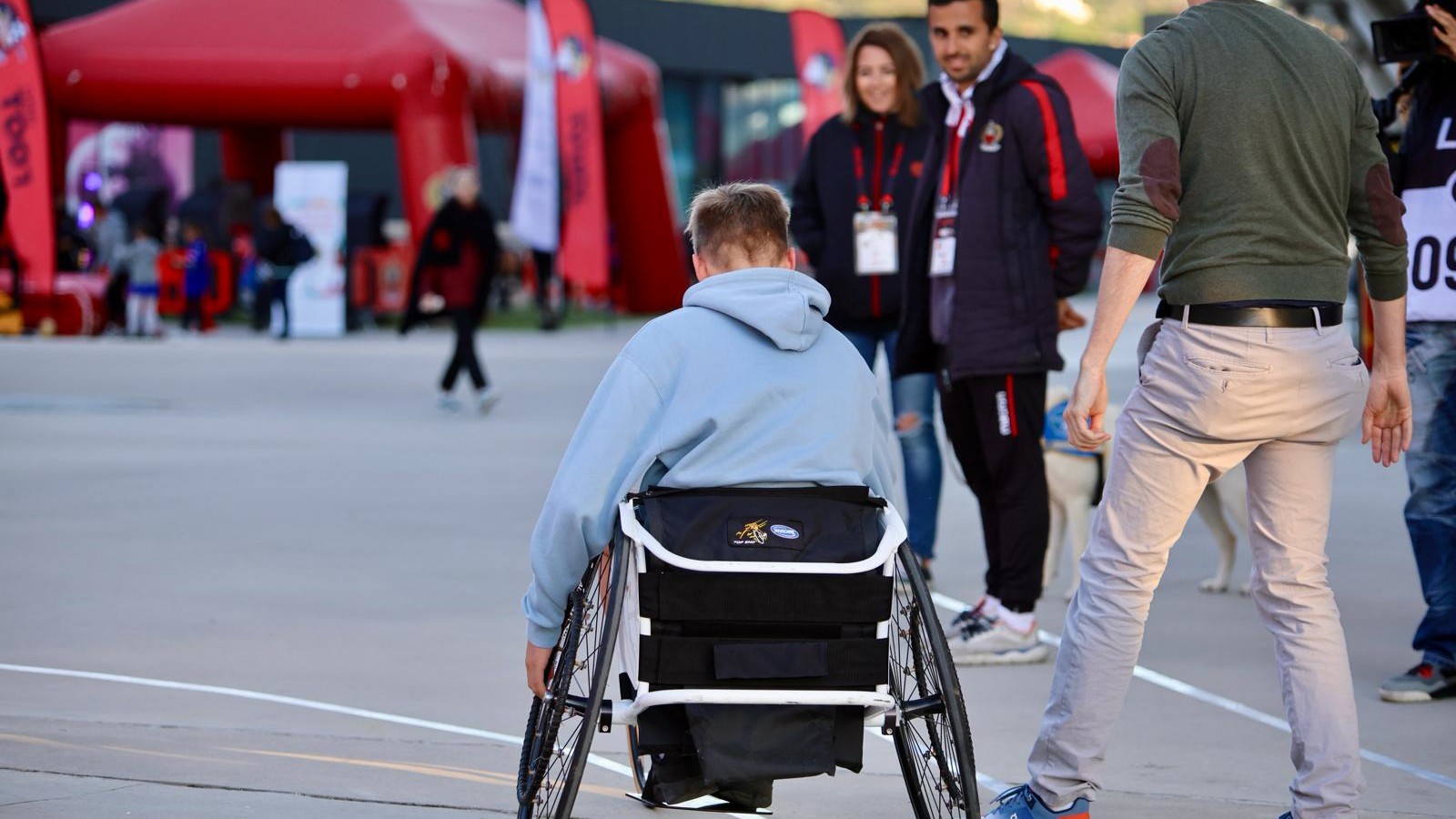 : Photo de sensibilisation au para-athlétisme sur le parvis de l'Allianz Riviera, avec un athlète en fauteuil roulant et des supporters niçois