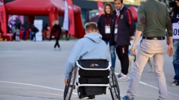 : Photo de sensibilisation au para-athlétisme sur le parvis de l'Allianz Riviera, avec un athlète en fauteuil roulant et des supporters niçois